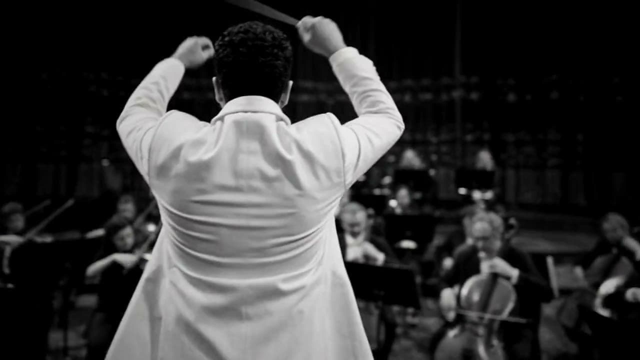 Un chef d'orchestre en veste blanche, de dos, face aux musiciens, en noir et blanc.